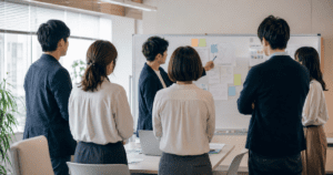 Japanese office team gathered around a whiteboard discussing a project together