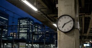 Are Japanese People Really Strict About "Time"? A Japanese train station clock in sharp focus, with late-night office windows blurred in the background, symbolizing different ways Japan treats time.